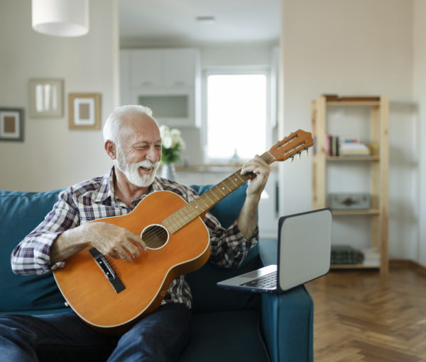 Elderly man learns to play acoustic guitar online using a Laptop