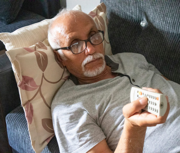 Senior man laying on couch with channel changer